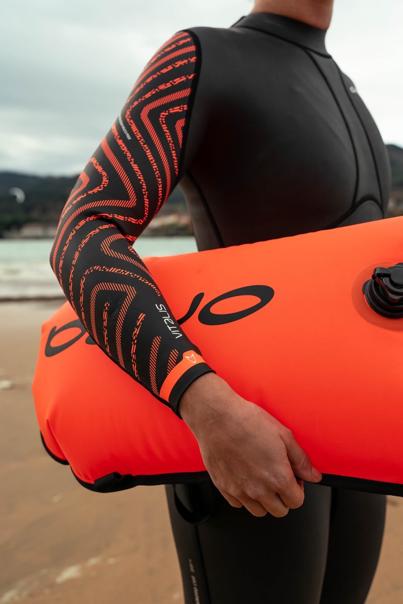 An open water swimmer poses in their Vitalis BS Orca wetsuit holding a swim safety buoy.