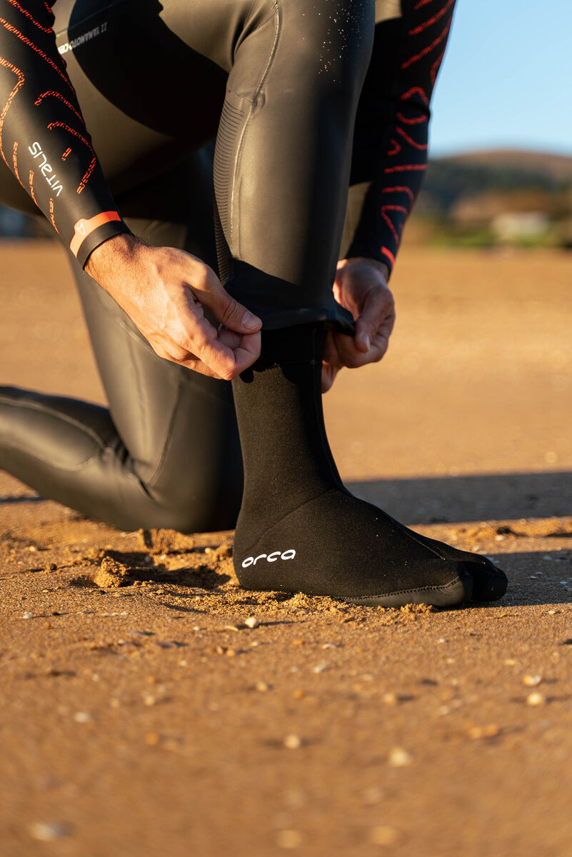 Person wearing a wetsuit and ORCA swimming socks on a beach