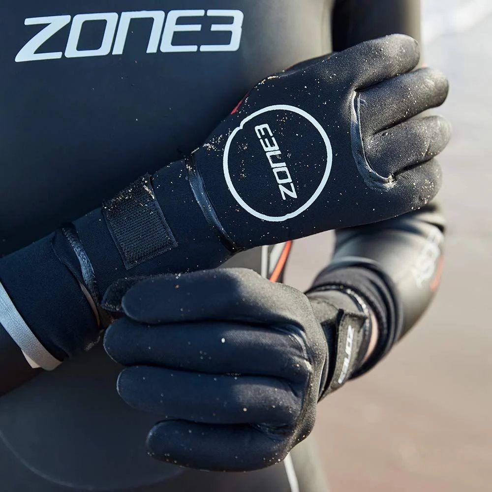 Athlete wearing Zone3 neoprene Heat-Tech swim gloves entering cold open water, demonstrating comfort and secure fit.