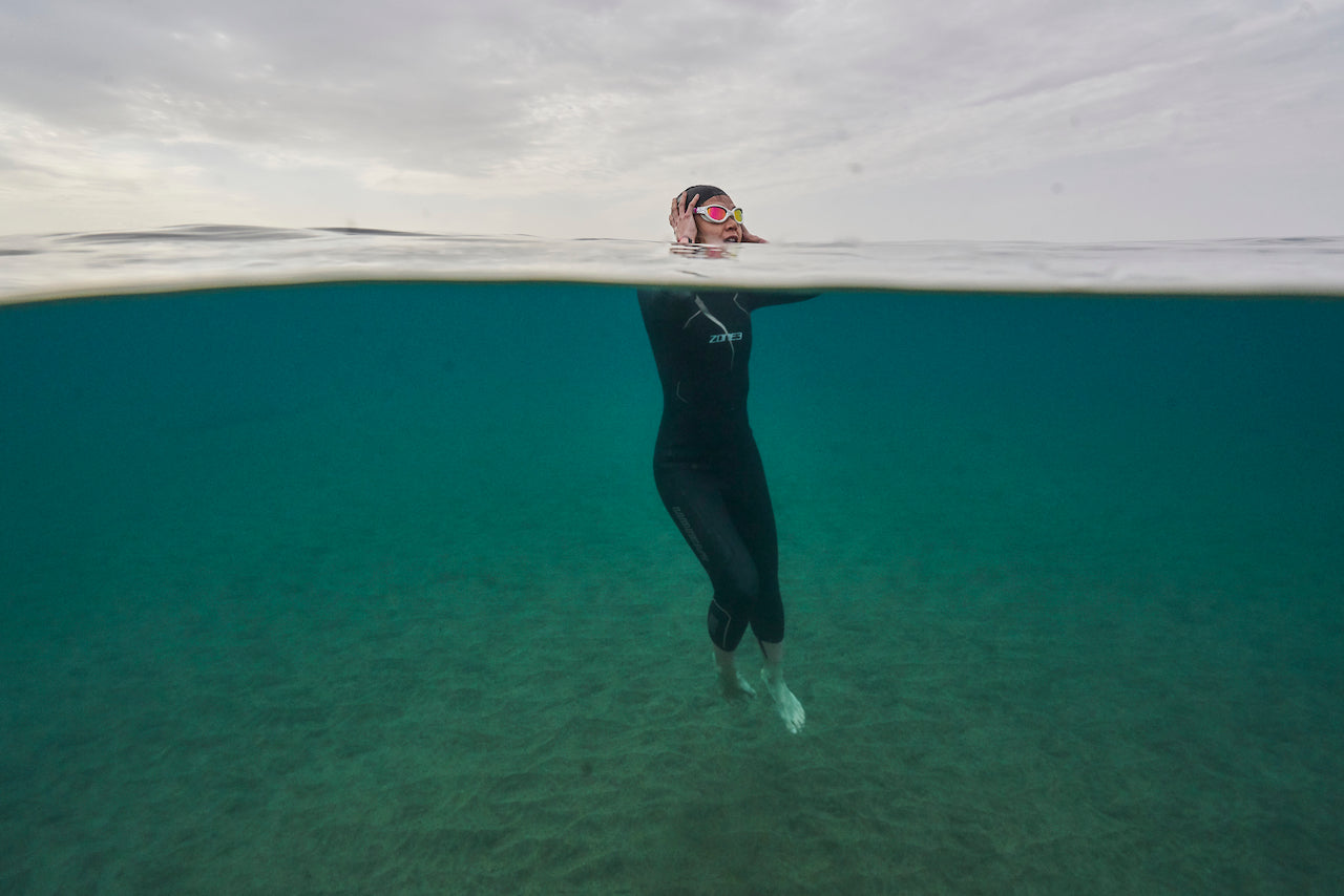 A triathlete floats in the water during a cold water swimming session wearing her neoprene accessories.