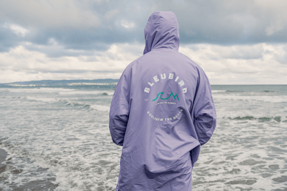Person wearing a lavender dry robe with 'BLEUBIRD' branding on a beach