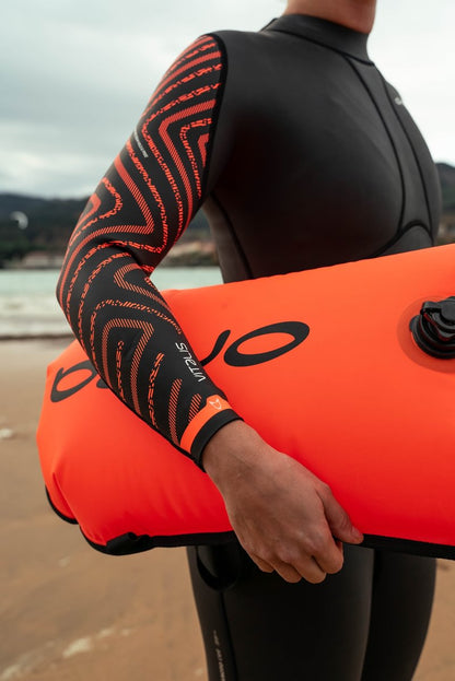 An open water swimmer poses in their Vitalis BS Orca wetsuit holding a swim safety buoy. 